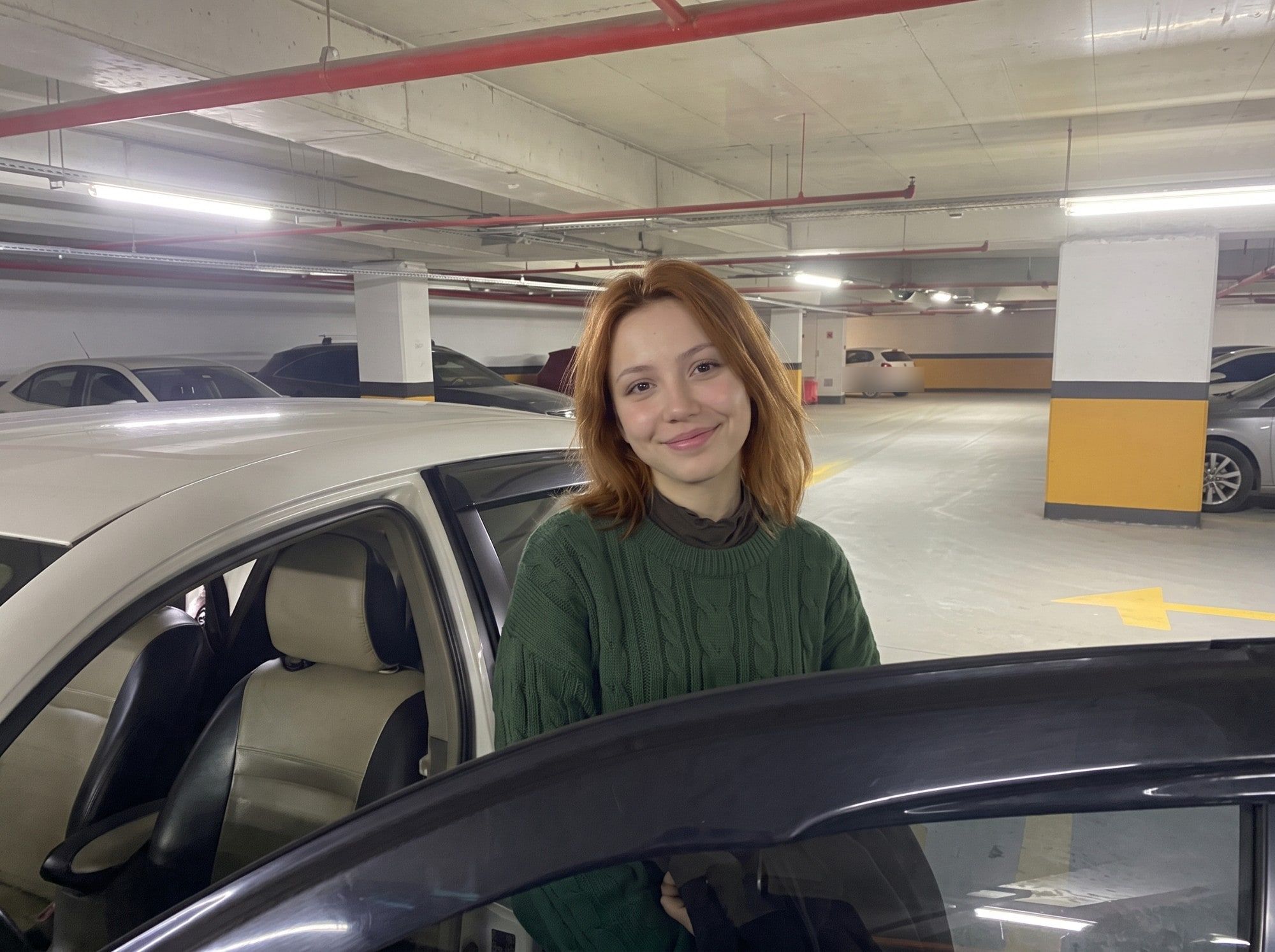 Kapalı otoparkta aracın kapısında gülümseyen öğrenci