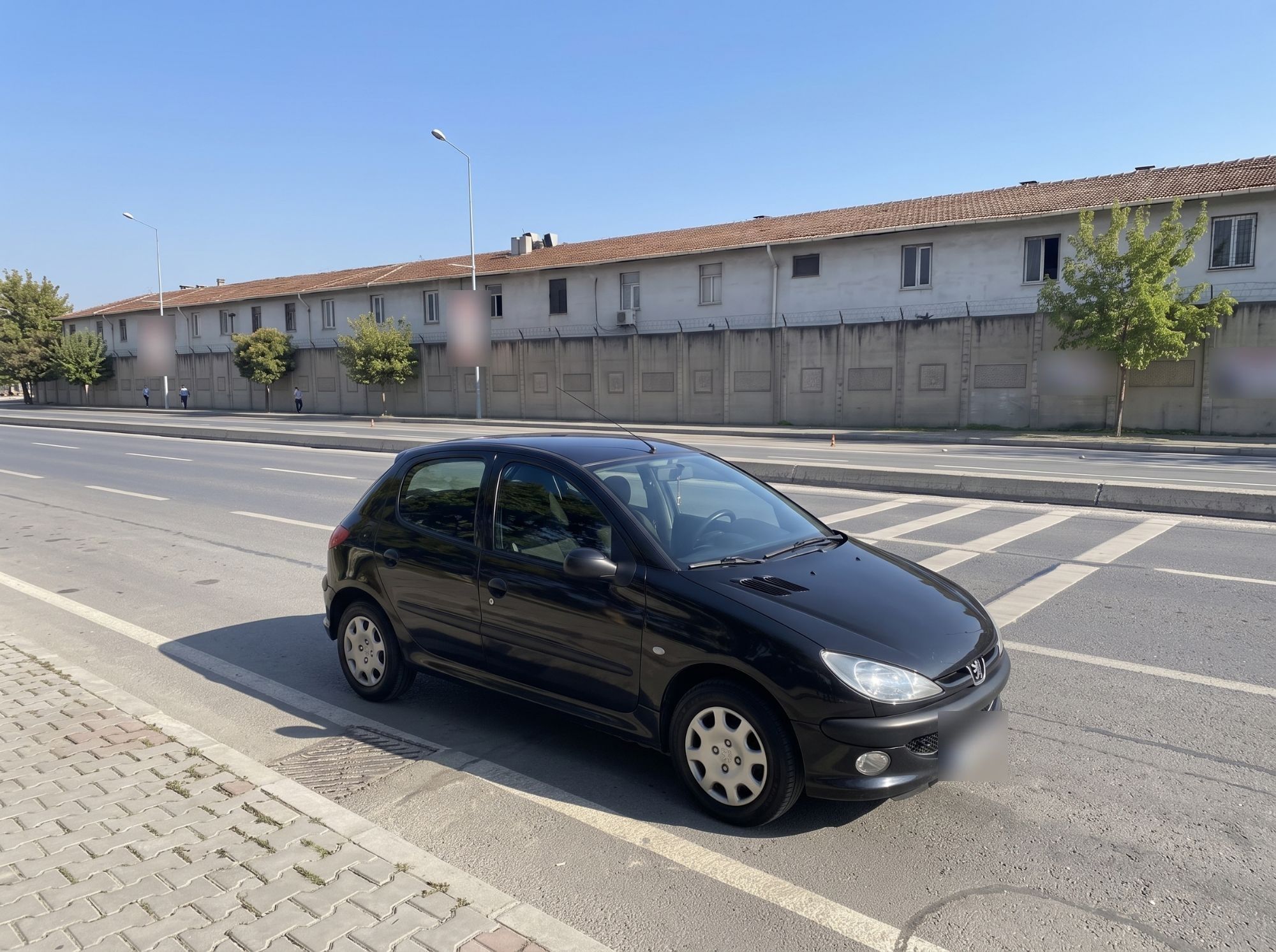 Ders aracı siyah Peugeot 206+, yol kenarında park hâlinde